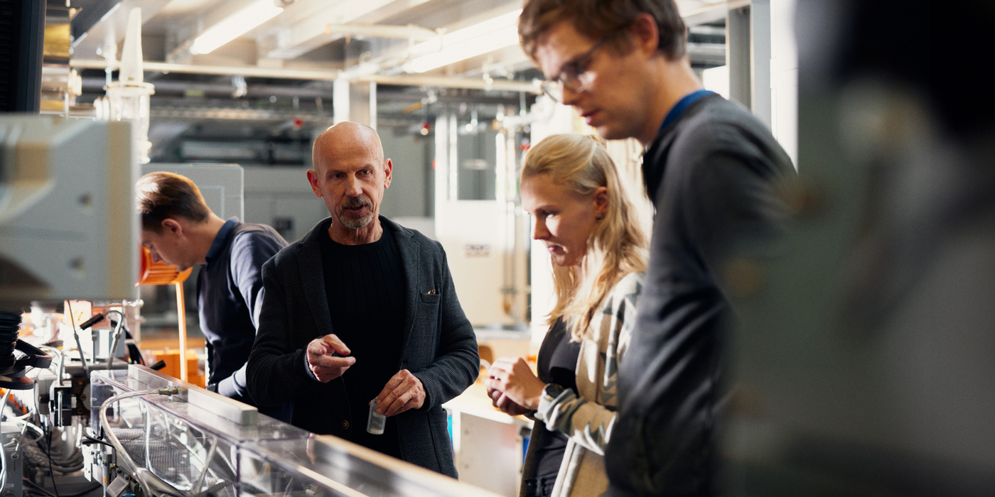 An der Doppelschneckenextruderanlage sieht man Johannes Brikmann der mit seinen Händen an einem Bedienelement schraubt Sein Blick ist konzentriert auf die Maschine gerichtet.