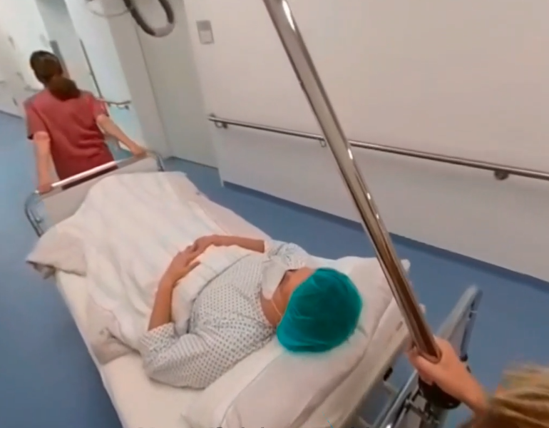 Zwei Pflegefachkräfte schieben das Bett des darin liegenden Patienten durch den Flur.