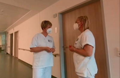 Zwei weibliche Pflegekräfte unterhalten sich auf einem Krankenhausflur.