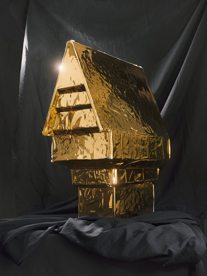 Foto eines in Goldfolie eingewickelten Modellhauses vor grauem Stoffhintergrund