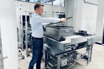 Ein Mann hebt den Deckel eines eckigen Waschbehälters in der Produktionslinie an.