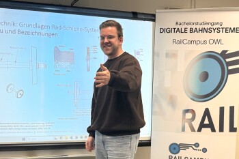 Ein junger steht vor einer Präsentationsfläche und macht eine freundliche und einladende Geste.