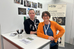 An einem Messestand stehen Catharina Schilp und Beatriz García. Im Hintergrund sieht man ein Roll-Up des Projekt InCamS@BI.
