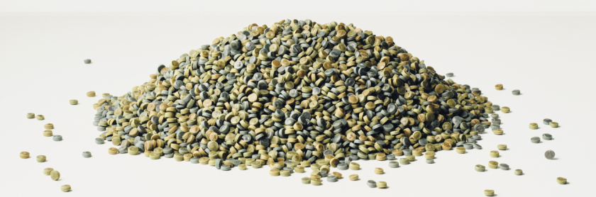 Grün-braune Kunststoff-Pellets auf einem Haufen vor weißem Hintergrund.