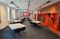 bild der Seminarräume in der Wissenswerkstadt der raum kann durch Teiilung auf bis zu 90 plätze erweitert werden auf dem bild sind die tische und stühle des raums zu acht gruppentischen zusammengestellt im hintergrund ist die große videoleinwand zu sehen.