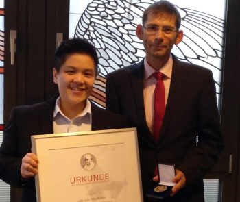 Preisträgerin mit Urkunde und Laudator mit Medaille