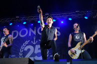 Zwei Männer mit Gitarre auf einer Bühne, in der Mitte hält ein Mann ein Mikro Richtung Publikum