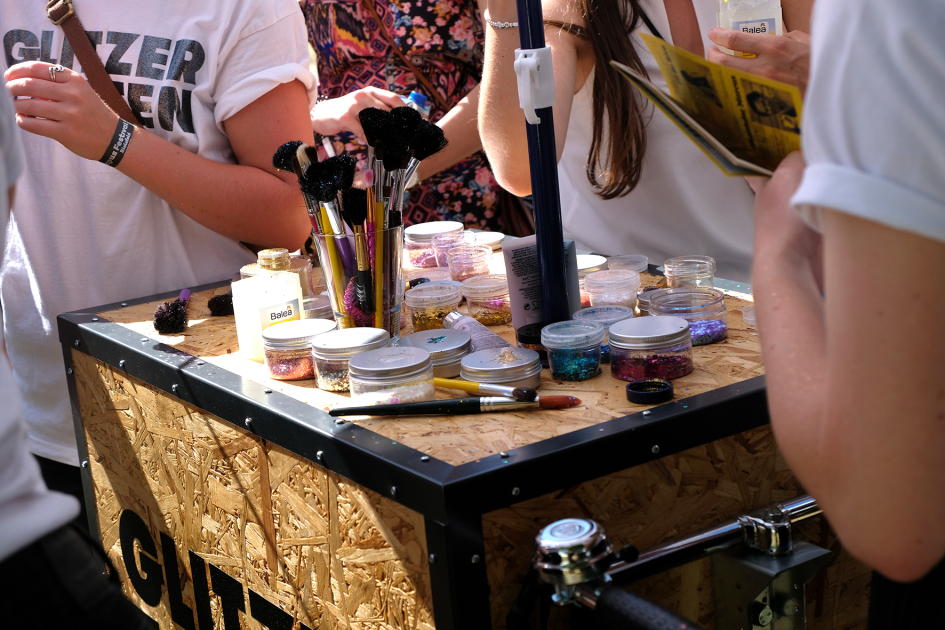 Verschiedene Pinsel und Behälter mit buntem Glitzer auf einer Holzbox