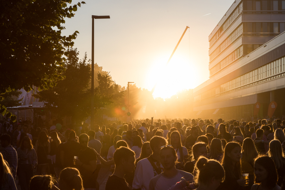 Eine Menschenmenge die im Hintergrund von der untergehenden Sonne bestrahlt wird.