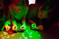 n einem abgedunkelten Raum der mit rotem und grünem Licht beleuchtet ist, versuchen Kinder ein Puzzle zu legen