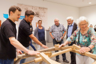 Sechs Personen schauen sich eine Holzbrücke an