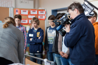 Eine Kamerafrau filmt neben einem Krankenbett, im Hintergrund stehen die Teilnehmer des Boys' day.