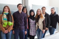 Sieben Studierende stehen nebeneinander vor einer Tafel.