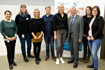 Acht Personen stehen nebeneinander und blicken in die Kamera.