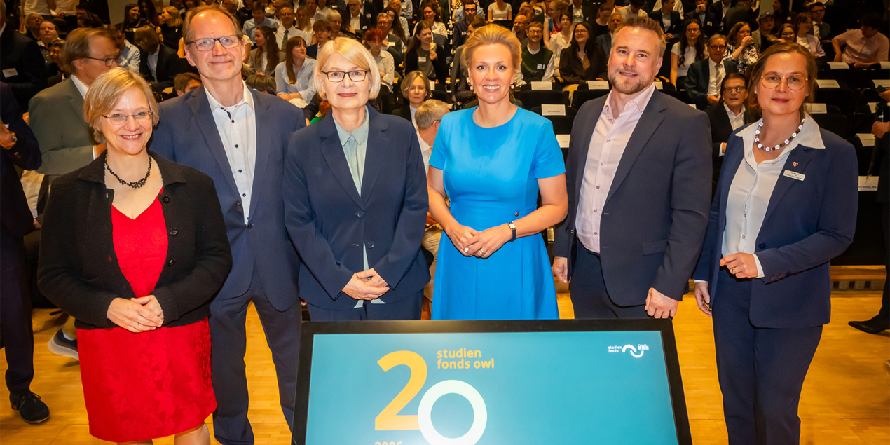 Foto: Sechs Personen stehen hinter einem Bildschirm auf dem 20 Jahre Studienfonds steht im Hintergrund sieht man die Gäste
