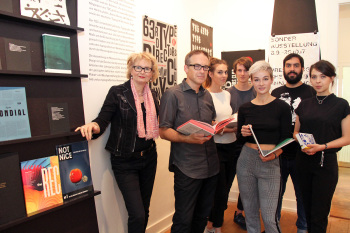 Die sieben Personen stehen in der Ausstellung und halten Bücher in ihren Händen.