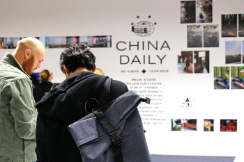 Zwei Personen stehen vor einer Wand mit Bildern.