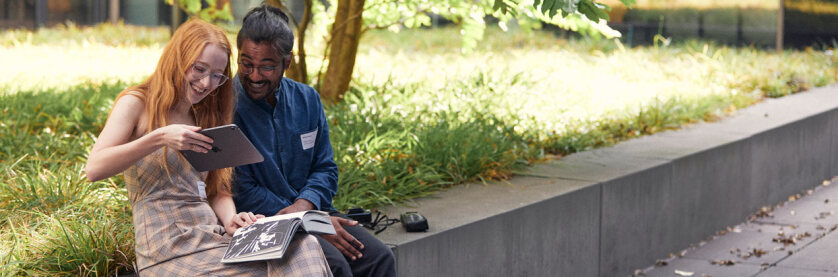 Eine Frau und ein Mann sitzen im Innenhof der FH Bielefeld und scannen mit einem Tablet eine Buchseite der Festschrift ein