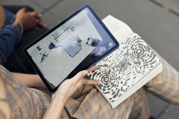 Eine Frau scannt mit einem Tablet eine Seite der Jubiläumsfestschrift ein