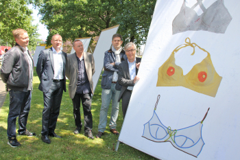 Die Männer stehen links von einem großen Plakat, auf dem drei Bikinioberteile abgebildet sind.