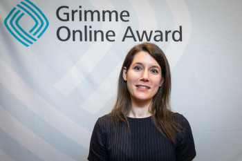 Eine Frau steht vor einer Wand und blickt in die Kamera.