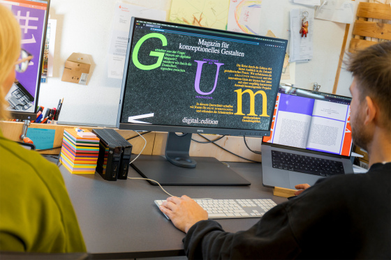 Menschen sitzen vor einem Bildschirm, darauf steht in großen bunten Buchstaben GUM