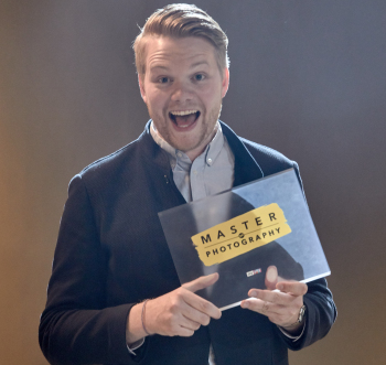 Ein Mann strahlt in die Kamera und hält eine Plexiglasscheibe in der Hand