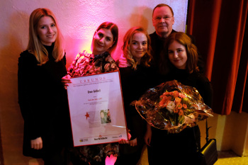 Fünf Personen, vier Frauen. Eine hält einen Bilderrahmen mit Urkunde in den Händen, eine einen Blumenstrauß.