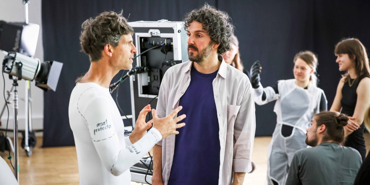 Prof Jan Burkhardt und Prof Philipp Rupp diskutieren miteinander Prof Burkhardt trägt ein enges weißes Kostüm