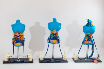 Drei blaue Schaufensterpuppen stehen nebeneinander, weiße Hände ziehen an Fäden um ihre Taille