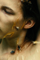 An einem Gesicht läuft Honig herunter. Darauf haben sich drei Bienen abgesetzt.