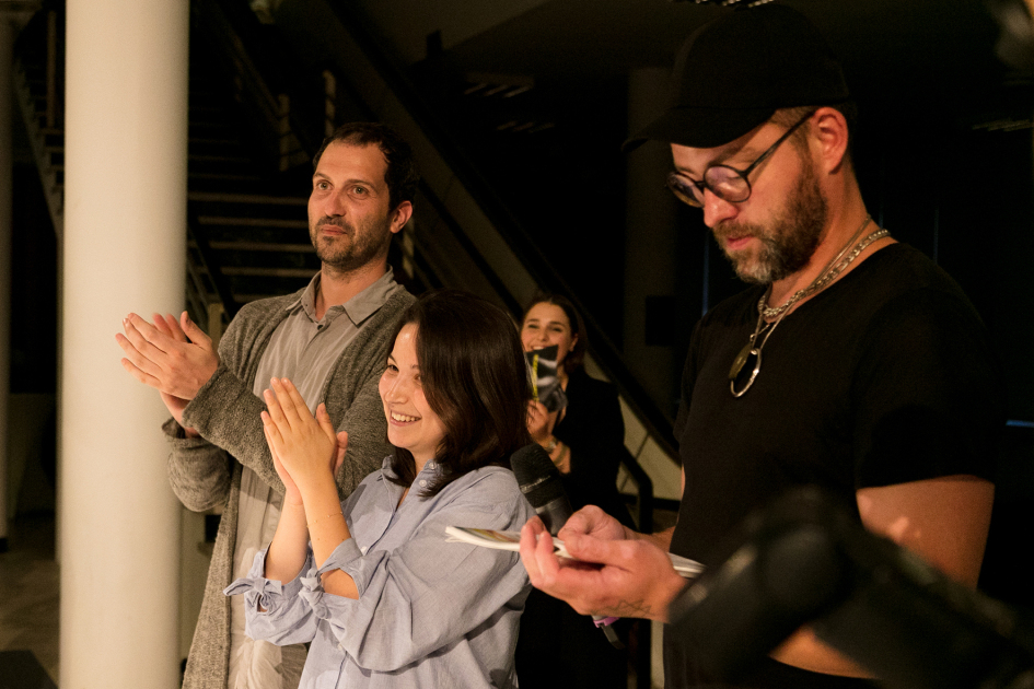 Drei Personen, eine Frau, stehen nebeneinander. Zwei von ihnen machen die Hände zu einer Klatschbewegung zusammen.