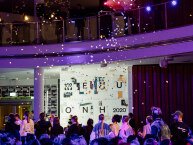 Menschen stehen unter einer Empore und Konfetti regnet auf sie herunter.