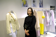 Eine Frau steht vor einer Kleiderstange mit hellen Kleidungssstücken