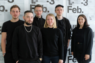 Vier Männer und zwei Frauen stehen vor einer Wand mit Plakaten der Werkschau