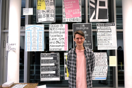 Ein Mann steht vor verschiedenen Postern mit Schriftzeichen und Slogans