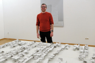 Ein Mann steht hinter einem Tisch mit kleinen Modellen aus Papier