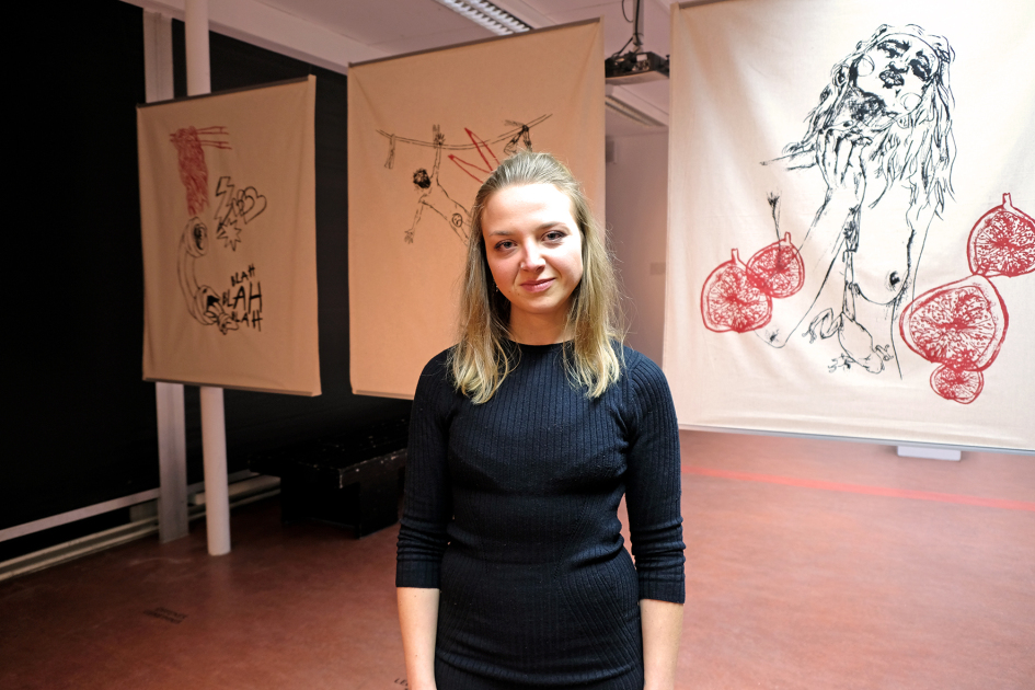 Eine Frau steht vor drei hängenden Stoffbahnen mit Zeichnungen