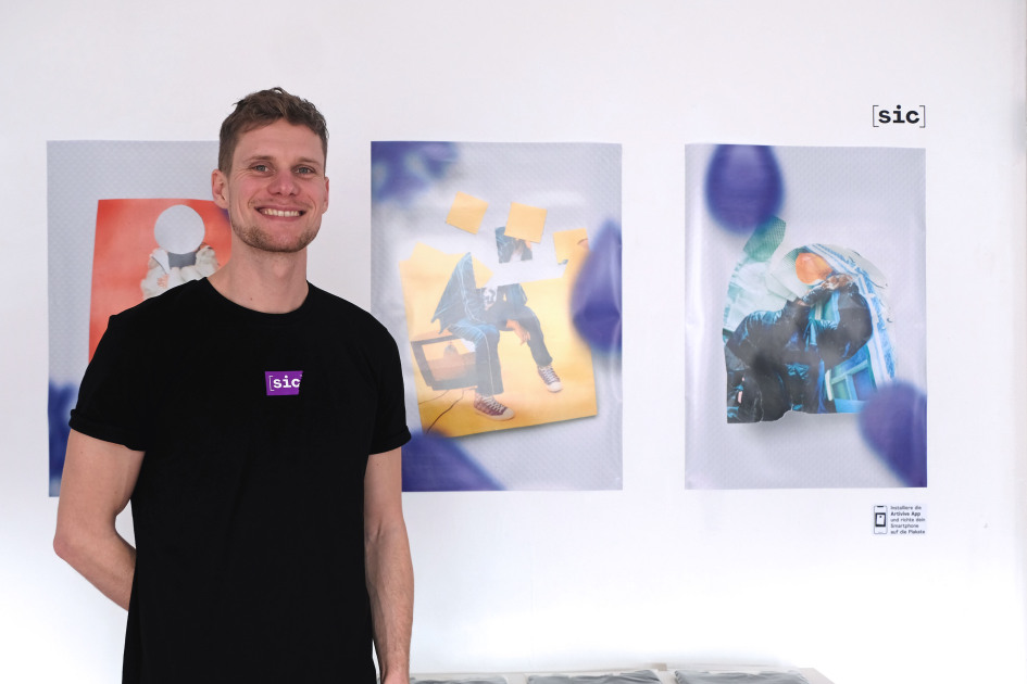 Ein Mann steht vor einer Wand mit Plakaten.