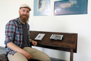 Ein Mann sitzt auf einer Bank an einem Pult.