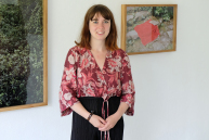 Eine Frau steht vor einer Wand, an der zwei Fotos hängen.