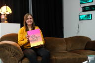 Eine Person sitzt auf einem Sofa und blickt in die Kamera.