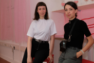 Zwei Personen lehnen an Barhockern und blicken in die Kamera.