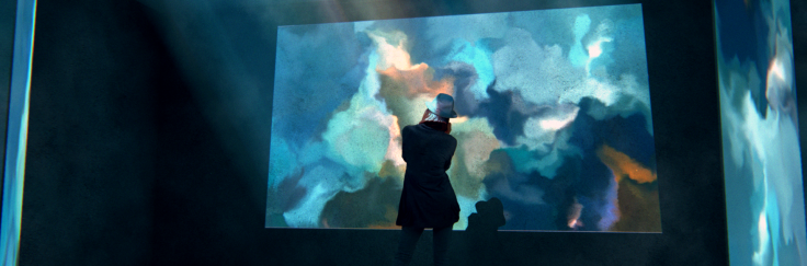 Eine Person steht in einem abgedunkelten Raum. Auf den Wänden sind unförmige Projektionen