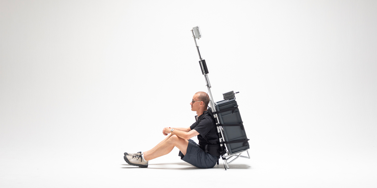 Foto: Ein Mann sitzt auf dem Boden und trägt einen Rucksack, der aus einem Koffer besteht.
