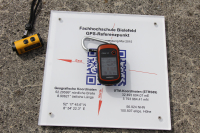 Die Platte mit den Koordinaten ist zu sehen. Auf ihr liegt ein GPS-Navigationsgerät.
