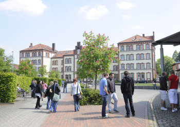 Einige Studierende stehen vor dem Hörsaalgebäude, im Hintergrund ist das Hauptgebäude zu sehen