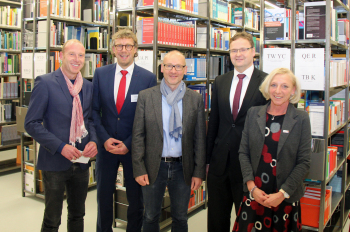 Vier Männer und eine Frauen stehen vor vollen Buchregalen in einer Bibliothek