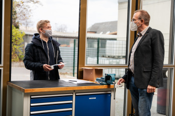Zwei Männer stehen sich an einem Fenster gegenüber und unterhalten sich.