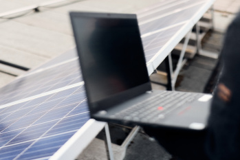 Eine Person hält einen Laptop, im HIntergrund sind Photovoltaikmodule zu sehen